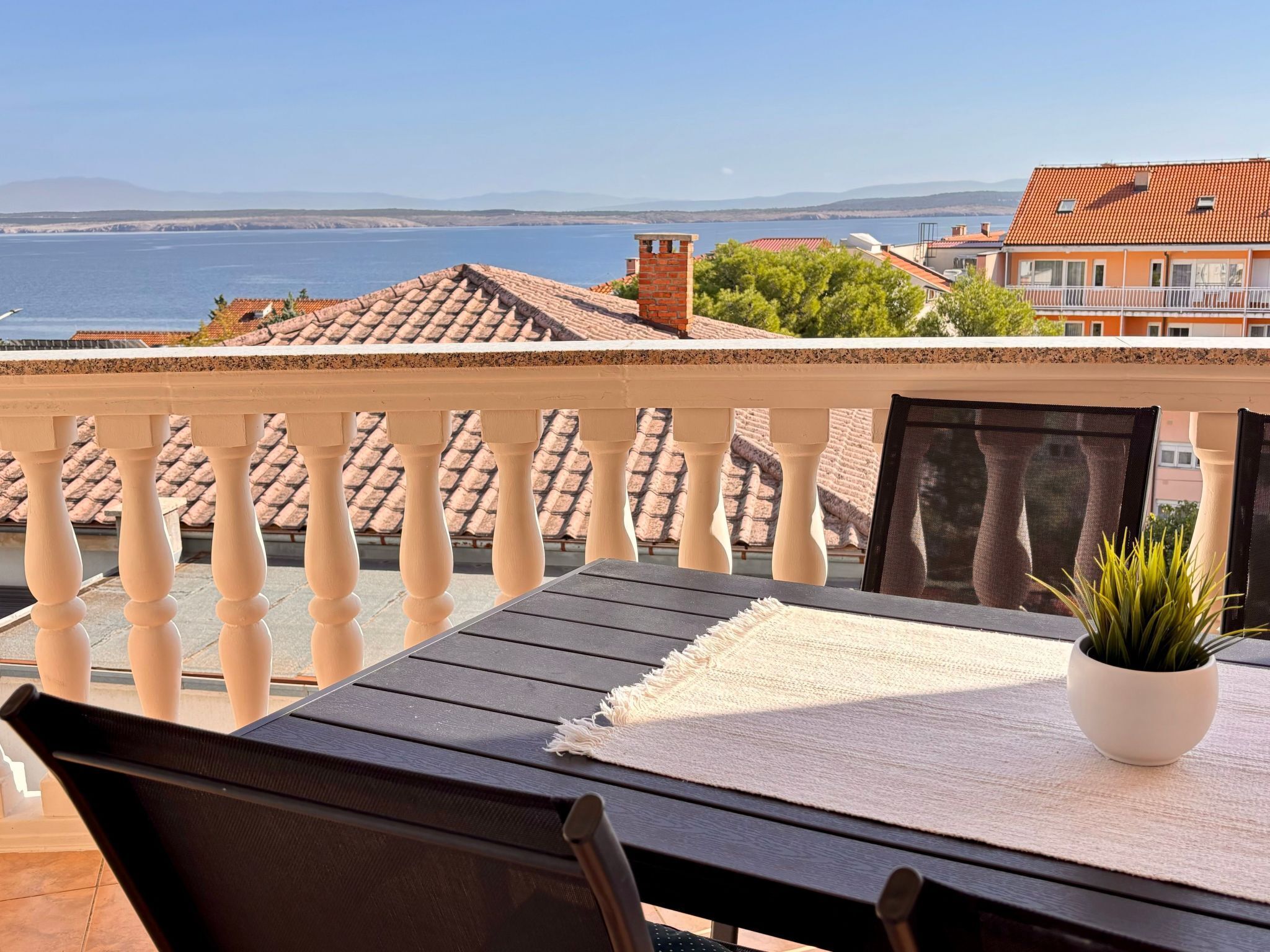 A balcony with a table and chairs, overlooking a body of water and buildings.