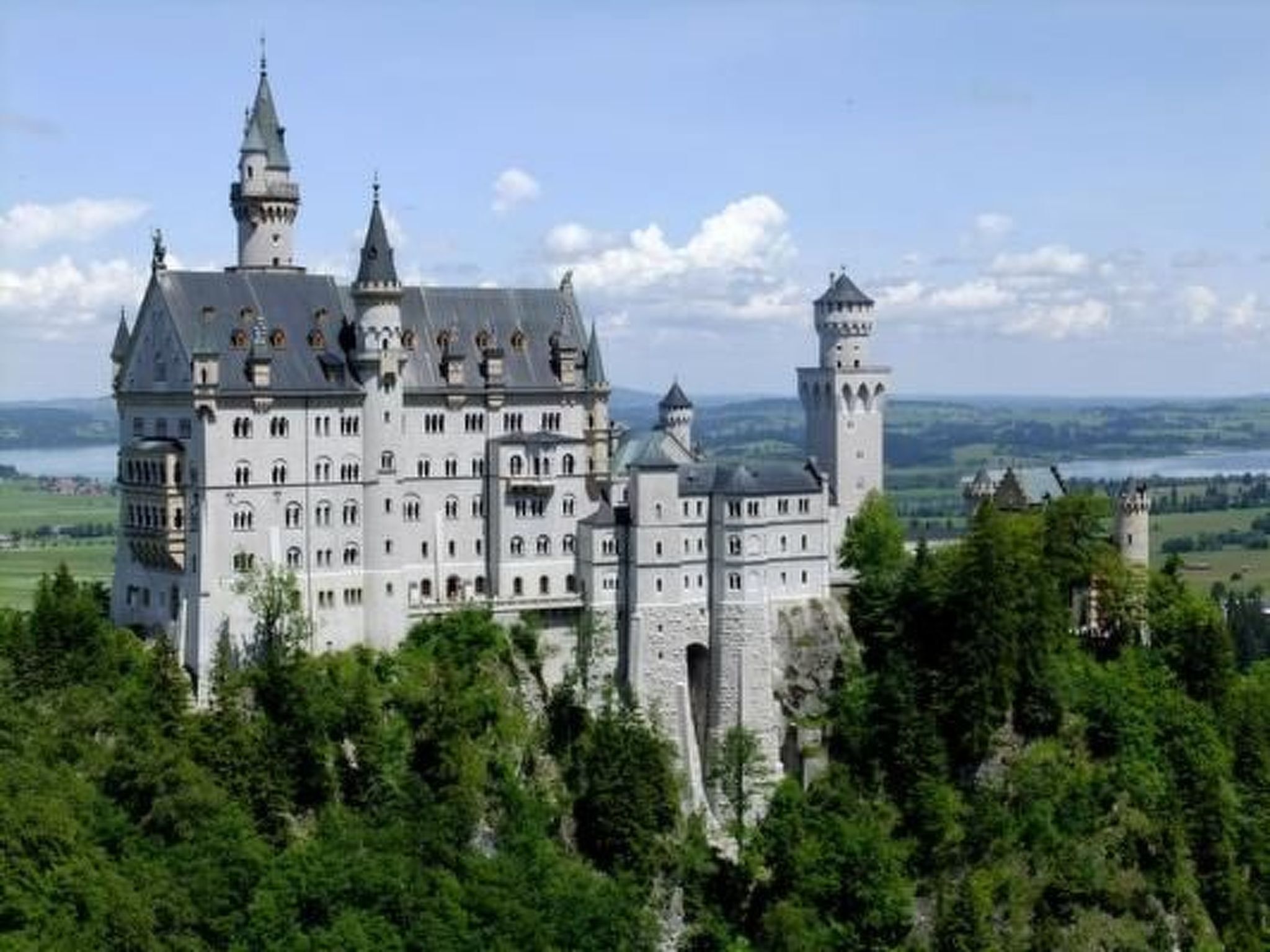 Un gran castillo histórico con múltiples torres y un edificio central destacado, rodeado de exuberante vegetación.