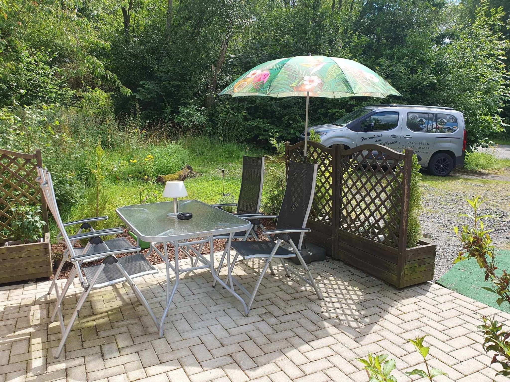 Une terrasse extérieure avec une table et des chaises, une clôture en bois et un fourgon stationné.