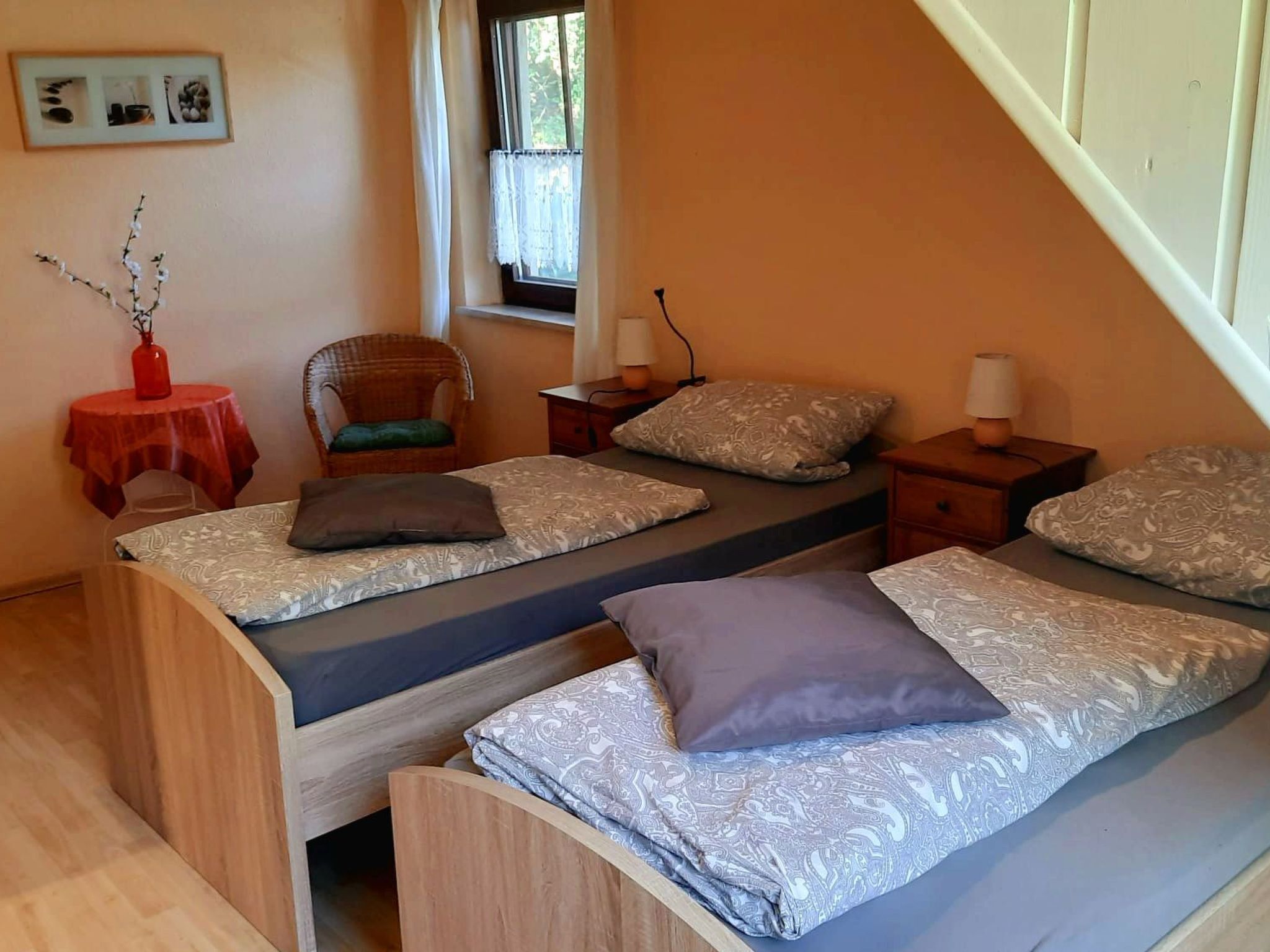 A bedroom with two beds, a chair, a small table, and a window.