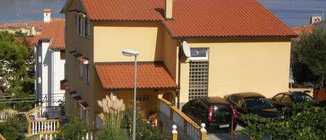A yellow building with a red roof, a staircase, and a parking area with cars.