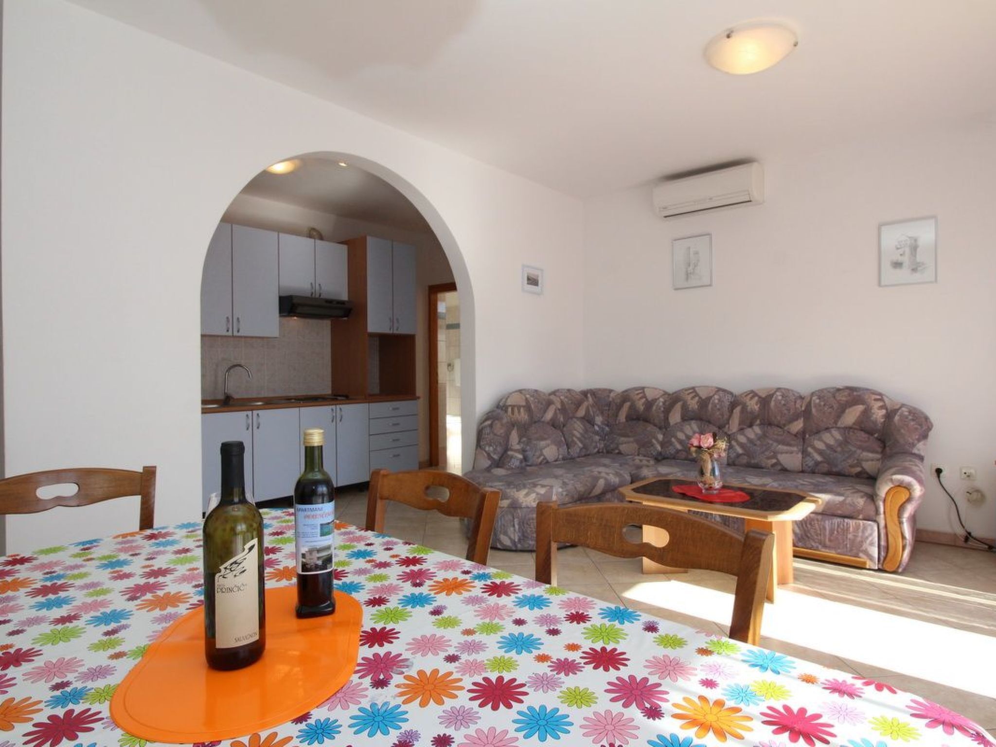 Un coin repas avec une table dressée pour deux personnes, un canapé et une porte en arc donnant sur la cuisine.