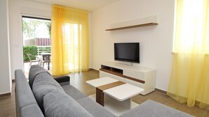 A modern living room with a grey sofa, a TV on a white cabinet, and yellow curtains. - Tolle Ferienwohnung in Baška mit Eigener Terrasse by Interhome (Krk/Baška)