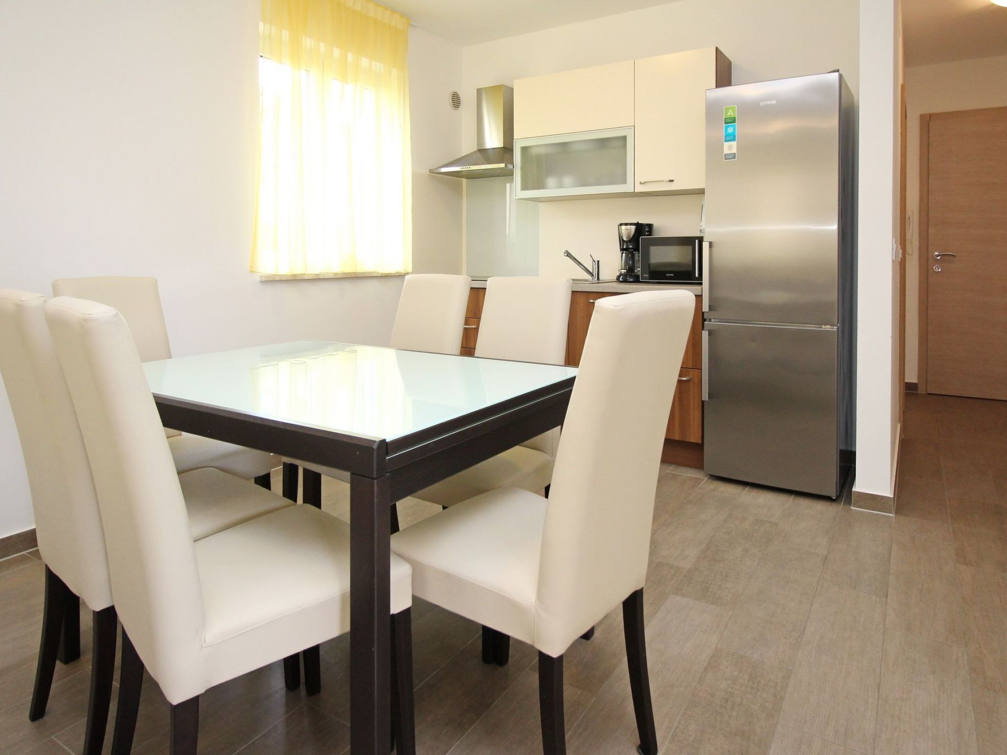 A modern kitchen with a dining table, chairs, a refrigerator, and a microwave.