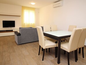 Una sala de estar moderna con televisor de pantalla plana, sofá gris y una mesa de comedor con seis sillas.