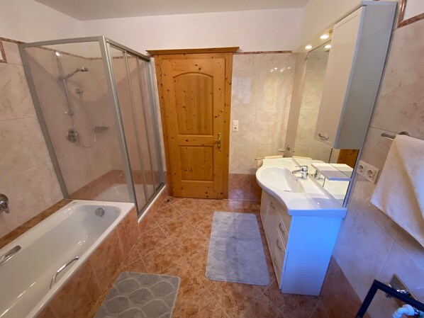 Casa de banho com chuveiro envidraçado, banheira, pia e porta de madeira.
