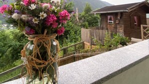Un florero de vidrio con arreglos florales en un balcón con vista a un paisaje montañoso.