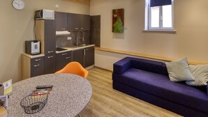 Eine moderne Küche mit dunklen Schränken, einem eingebauten Backofen und einem Fenster. Es gibt ein violettes Sofa und einen runden Tisch mit einem Korb.