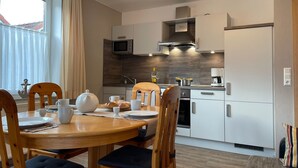 A modern kitchen with white cabinets, a microwave, and a stove. There is a dining table with chairs and a small window with curtains. - Helle Erdgeschosswohnung mit sonniger Terrasse by Interhome (Altfunnixsiel)