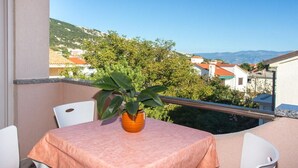 Ein Balkon mit Tisch und Stühlen, einer Topfpflanze und Blick auf eine Hügelstadt.