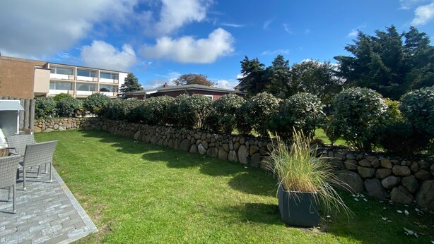 A courtyard with a stone wall, a grassy area, and a seating area with chairs. - in Wenningstedt-Braderup (Sylt) by Interhome (Wenningstedt-Braderup)