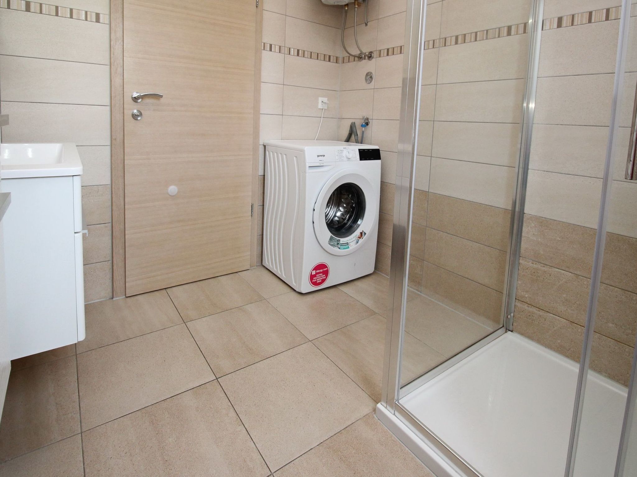A bathroom with a washing machine, a shower, and a sink.