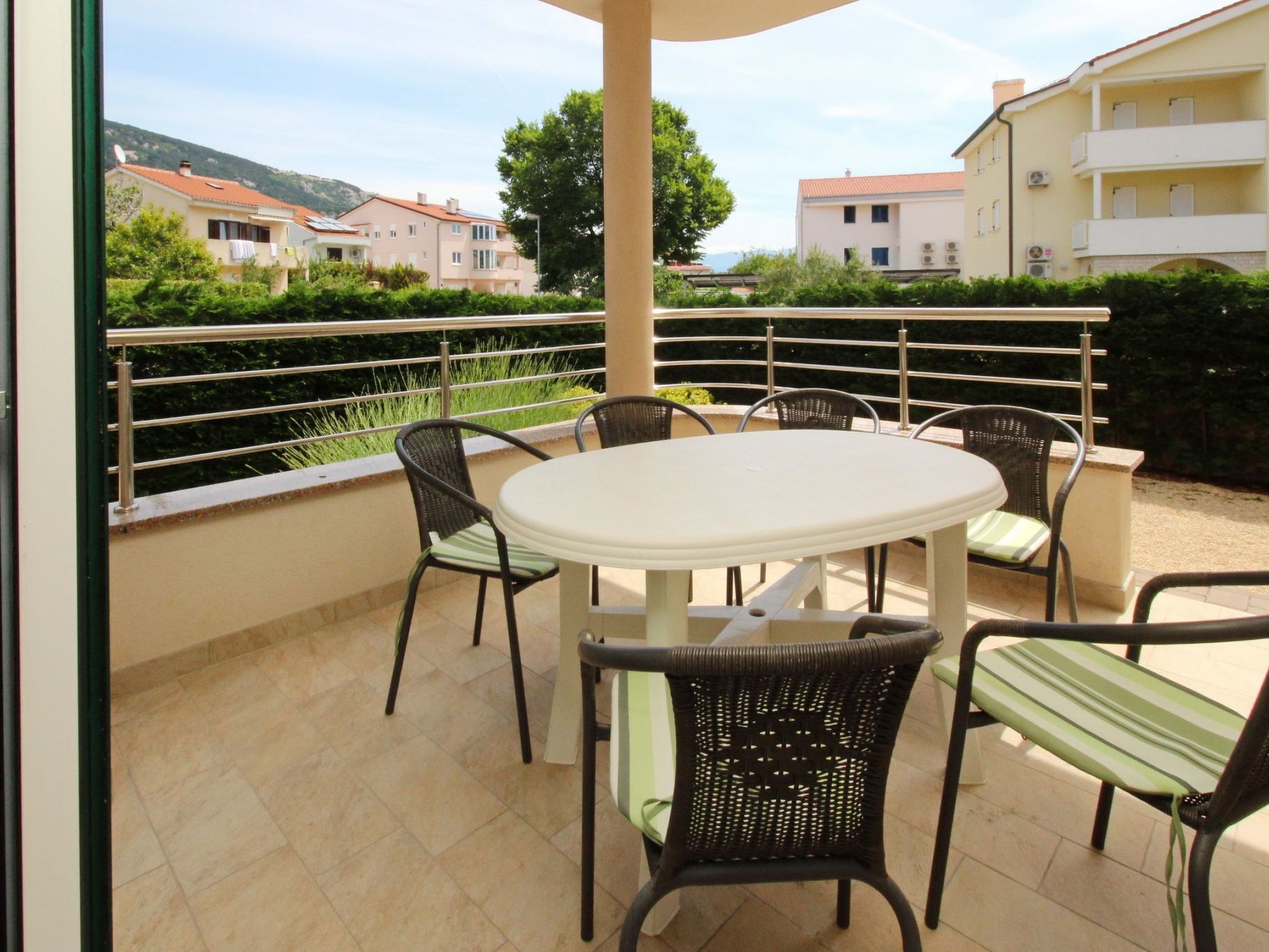 A balcony with a round table and chairs, overlooking a residential area with houses and greenery.