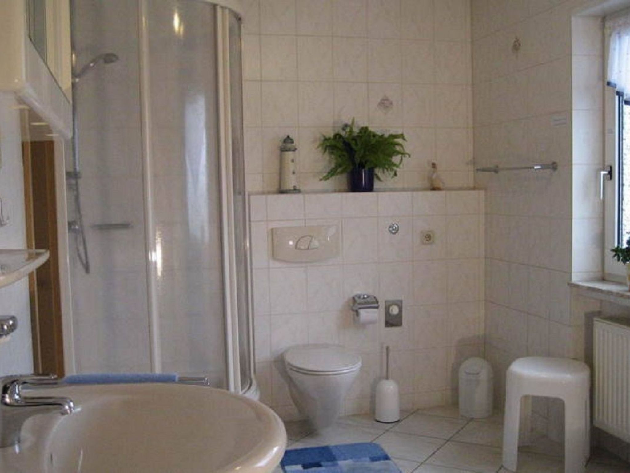 Et badeværelse med bruser, toilet, håndvask og en lille plante på væggen.