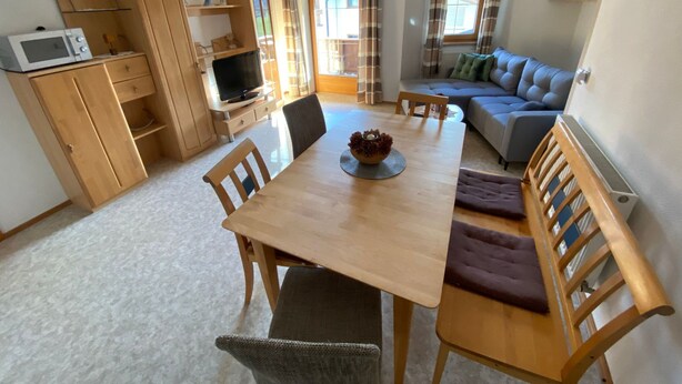 A dining area with a wooden table, chairs, and a television. There is a sofa and a window with curtains. - App. Gabriela by Interhome (Kaltenbach)