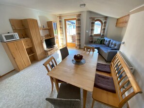 En matplats med ett träbord, stolar och en tv. Det finns också en soffa och ett fönster med gardiner.