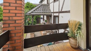 A balcony with a wooden floor, a brick wall, and a view of a house with a tiled roof and a hanging plant. - Haus-Fernblick by Interhome (Mechernich)