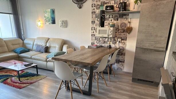A modern living room with a wooden dining table, white chairs, a beige sofa, and a colorful rug. - Feriendomizil Adler by Interhome (Goslar)