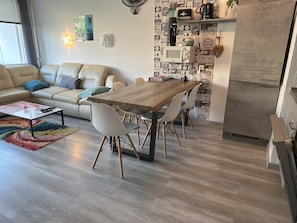 Un salon moderne avec une table à manger en bois, des chaises blanches, un canapé beige et un tapis coloré.
