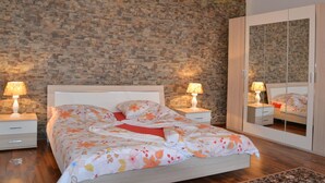 Una camera da letto con parete in pietra, un letto con lenzuola a motivi floreali, lampade ai comodini, un armadio e uno specchio.