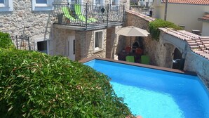 Un edificio in pietra con piscina, un balcone con una sedia verde e un piccolo tavolo da esterno con ombrellone.