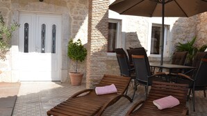 Un patio con poltroncine da esterno in legno, un tavolo e sedie, una pianta in vaso e una porta con pannelli di vetro.