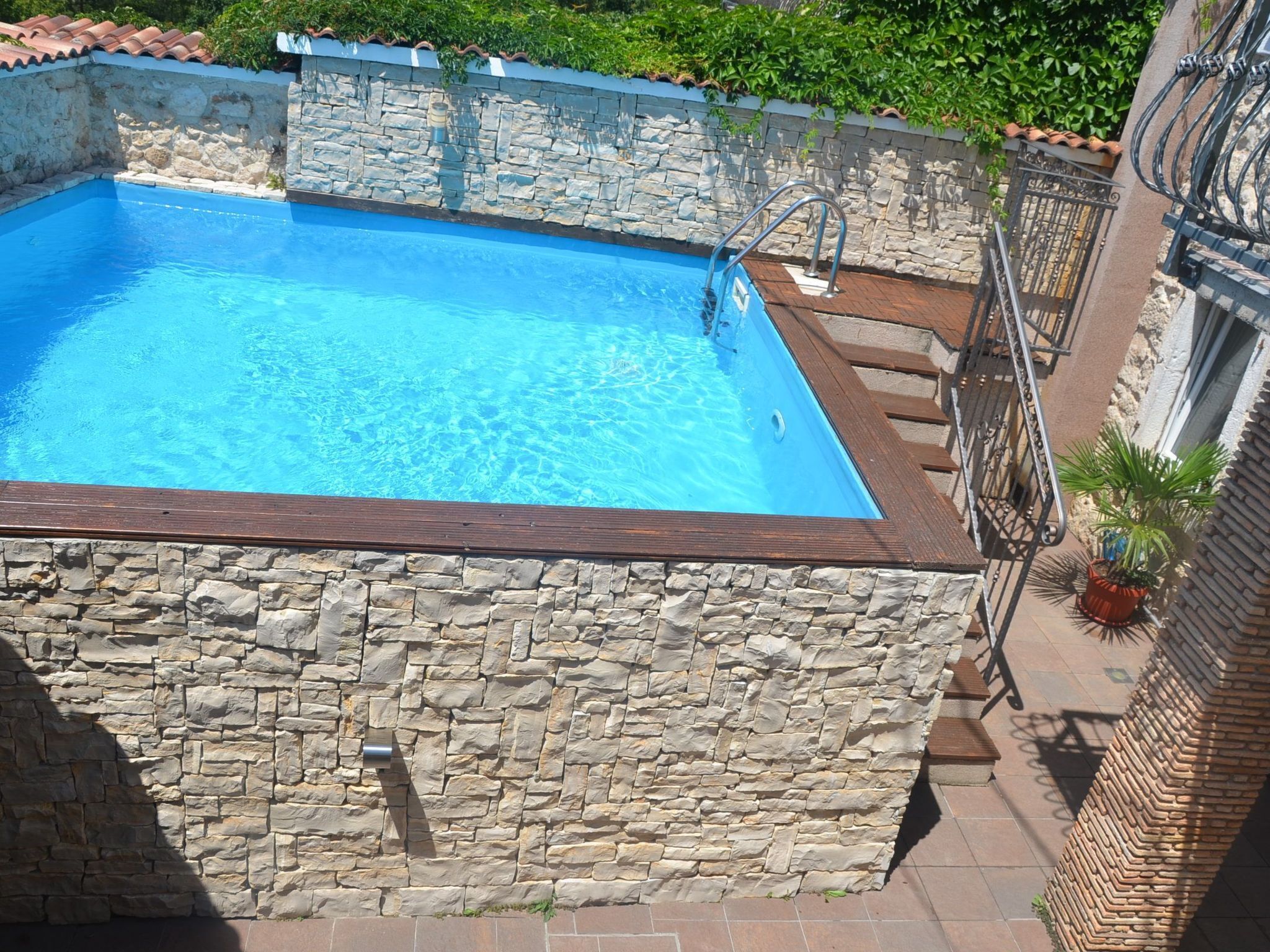 A rectangular swimming pool with stone walls and a wooden deck edge.