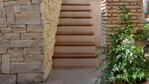 Una scala in pietra conduce a una porta, affiancata da muri in pietra e piante in vaso.