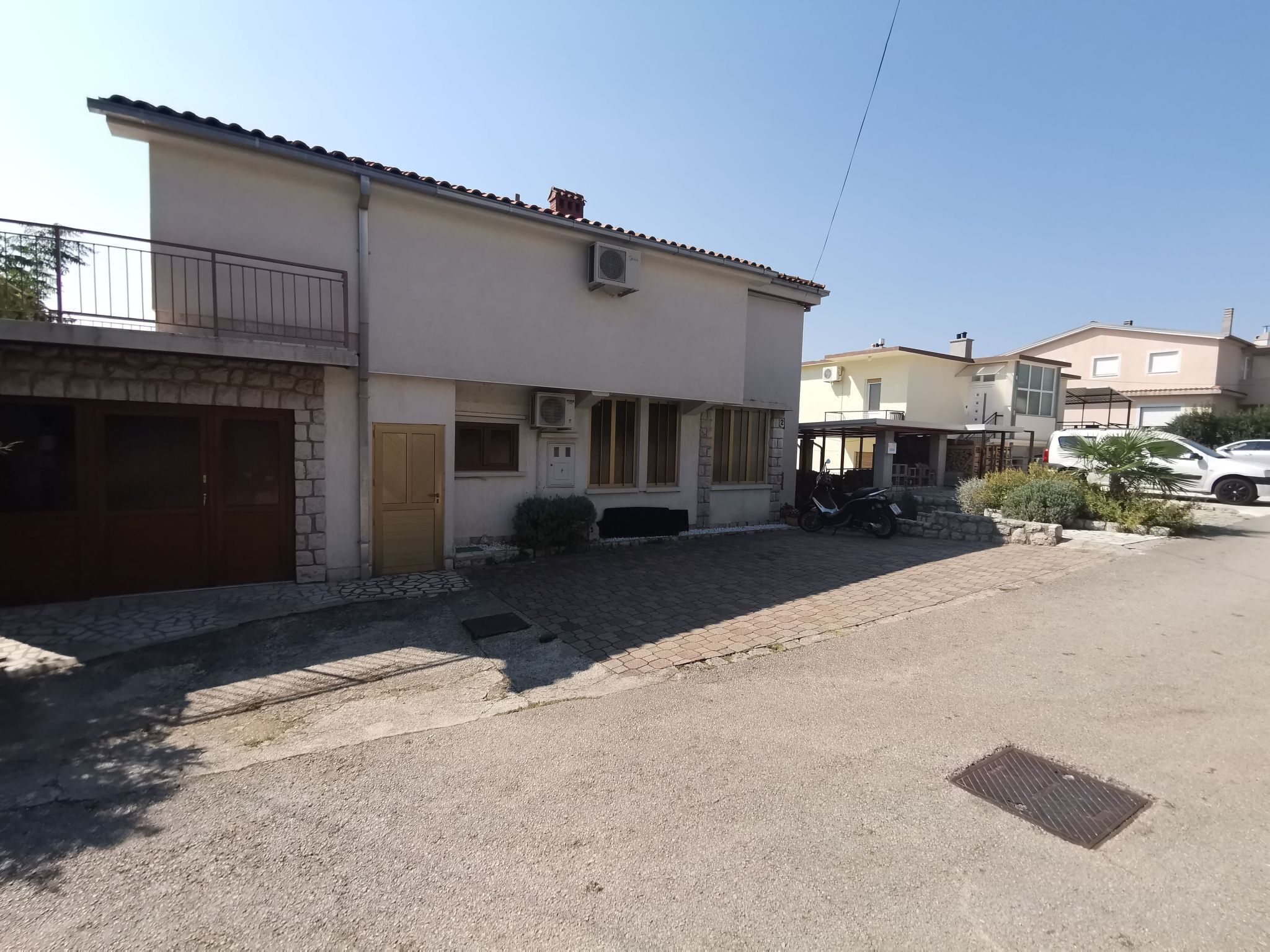 A residential street with houses, a paved driveway, and a parked scooter.