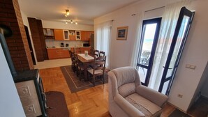 A modern living room with a sofa, a dining area with a table and chairs, a kitchen with wooden cabinets, and a large window with curtains. - Wohnung mit Terrasse und Meerblick by Interhome (Crikvenica)