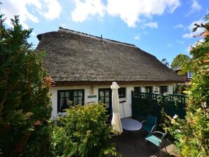 A thatched-roof cottage with a small patio area, a table, and chairs. - Lotsenhaus by Interhome (Baabe)