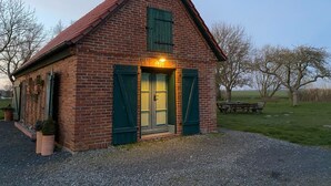 Ein kleines Backsteinhaus mit geneigtem Dach und grünen Fensterläden, mit einem einladenden Eingang und einer Lampe über der Tür.