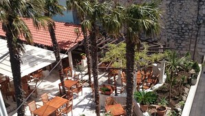Eine Außenpatio-Terrasse mit Holztischen und -stühlen, umgeben von Palmen und Kübelpflanzen.