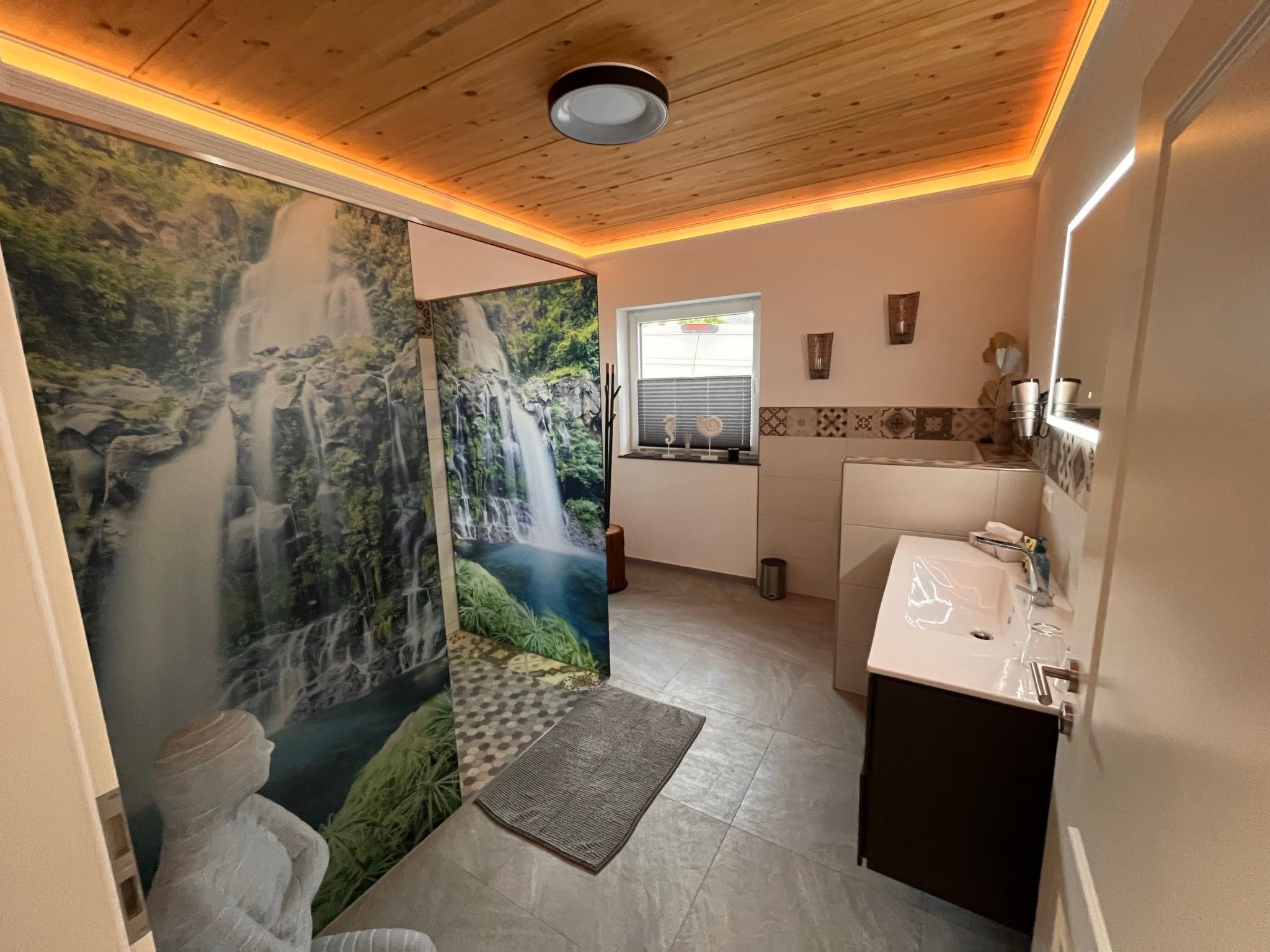 Ein Badezimmer mit Wandgemälde eines Wasserfalls, einem Waschbecken und einem Fenster mit Jalousien.