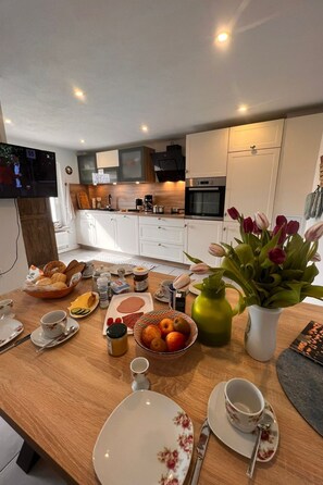 Una cocina moderna con armarios blancos, encimera de madera y un comedor con platos, cuencos y un florero con tulipanes.