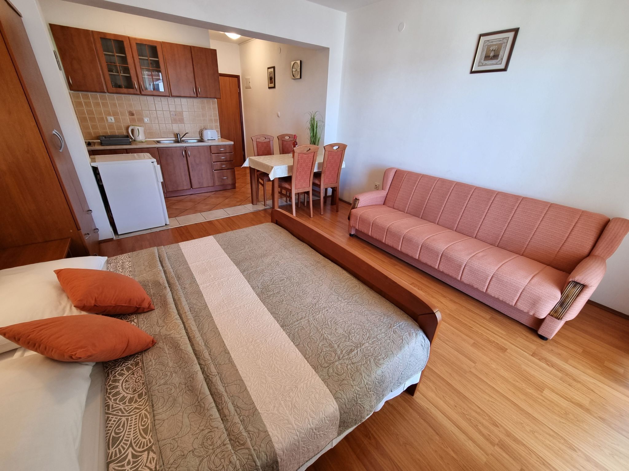 A bedroom with a bed, a sofa, and a kitchenette in the background.