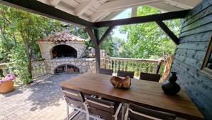 An outdoor patio with a stone fireplace, a wooden table with chairs, and a view of greenery. - VIL Studio-Wohnung in Crikvenica, Kvarner Bucht by Interhome (Crikvenica)