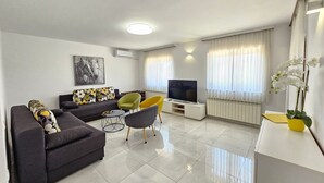 Uma sala de estar moderna com sofá, cadeiras, televisão e um vaso com planta.