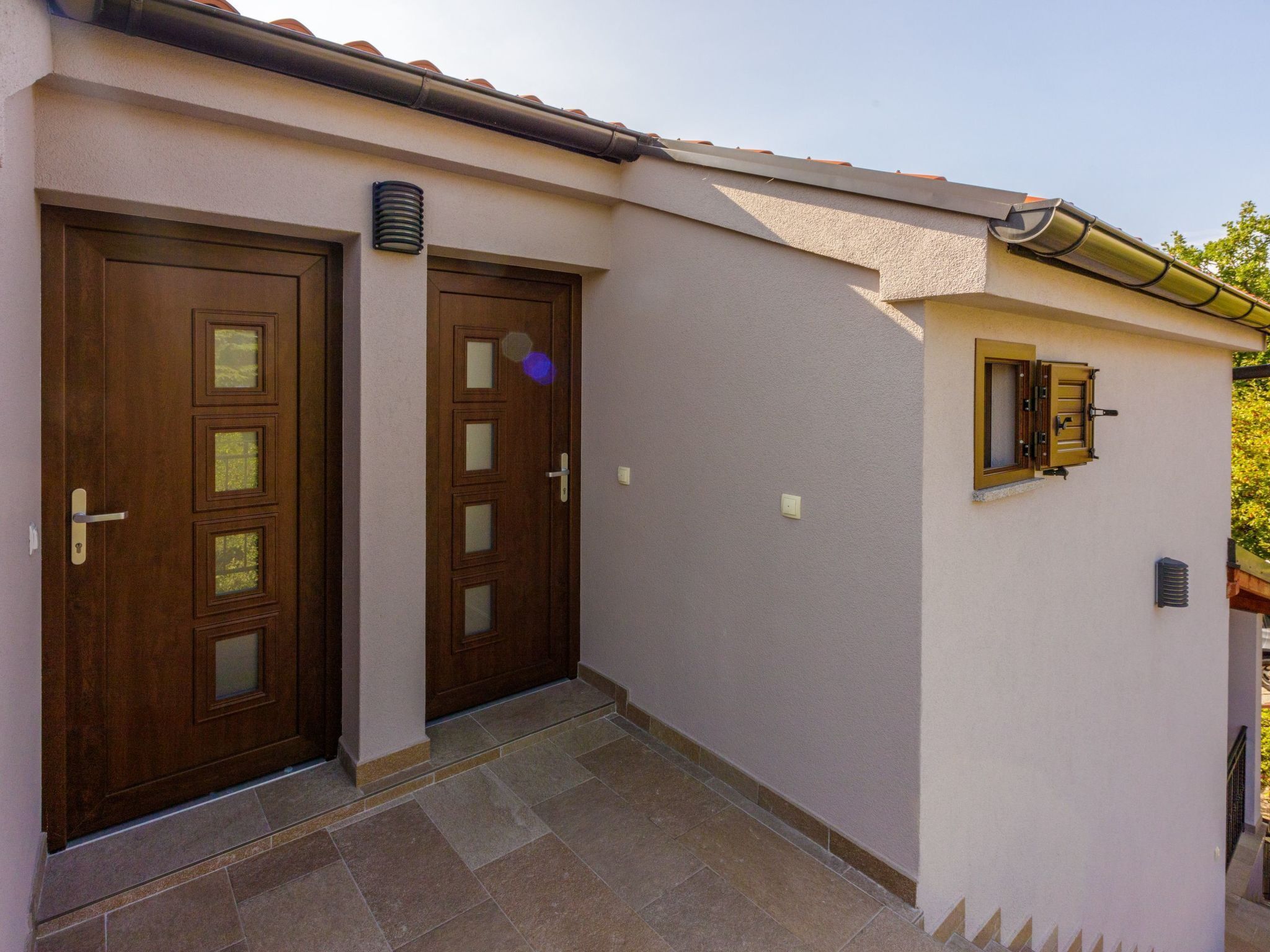 A building with two wooden doors, a small window, and a tiled entrance area.