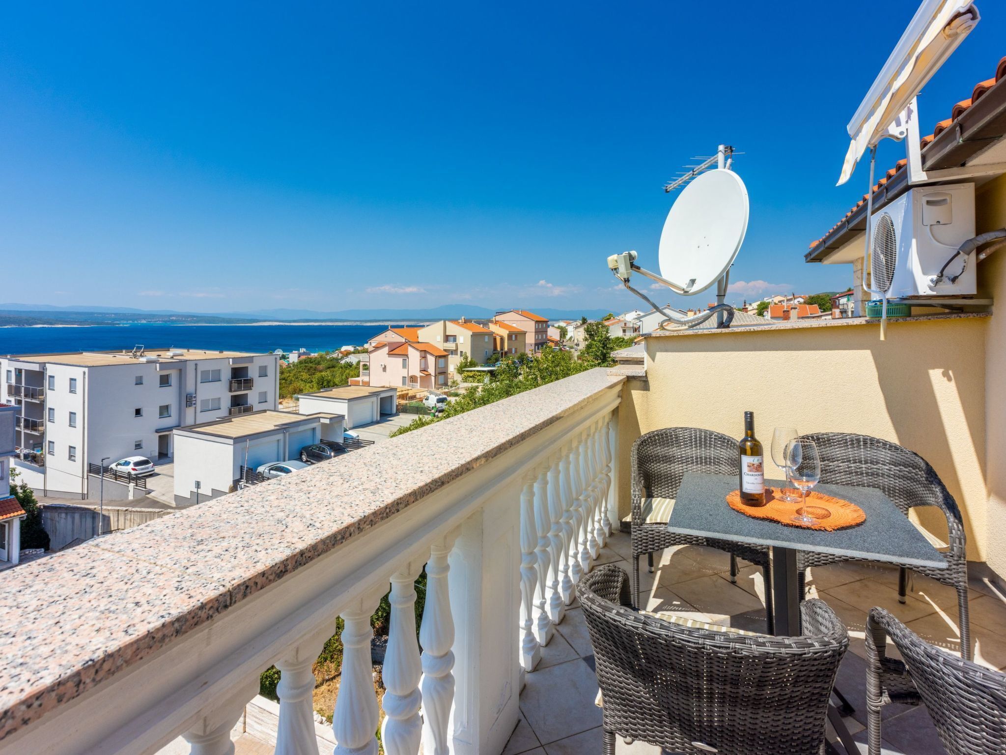 Ein Balkon mit Tisch und Stühlen, einer Satellitenschüssel und Blick auf das Meer und Gebäude.