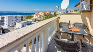 Ein Balkon mit Tisch und Stühlen, einer Satellitenschüssel und Blick auf das Meer und Gebäude.