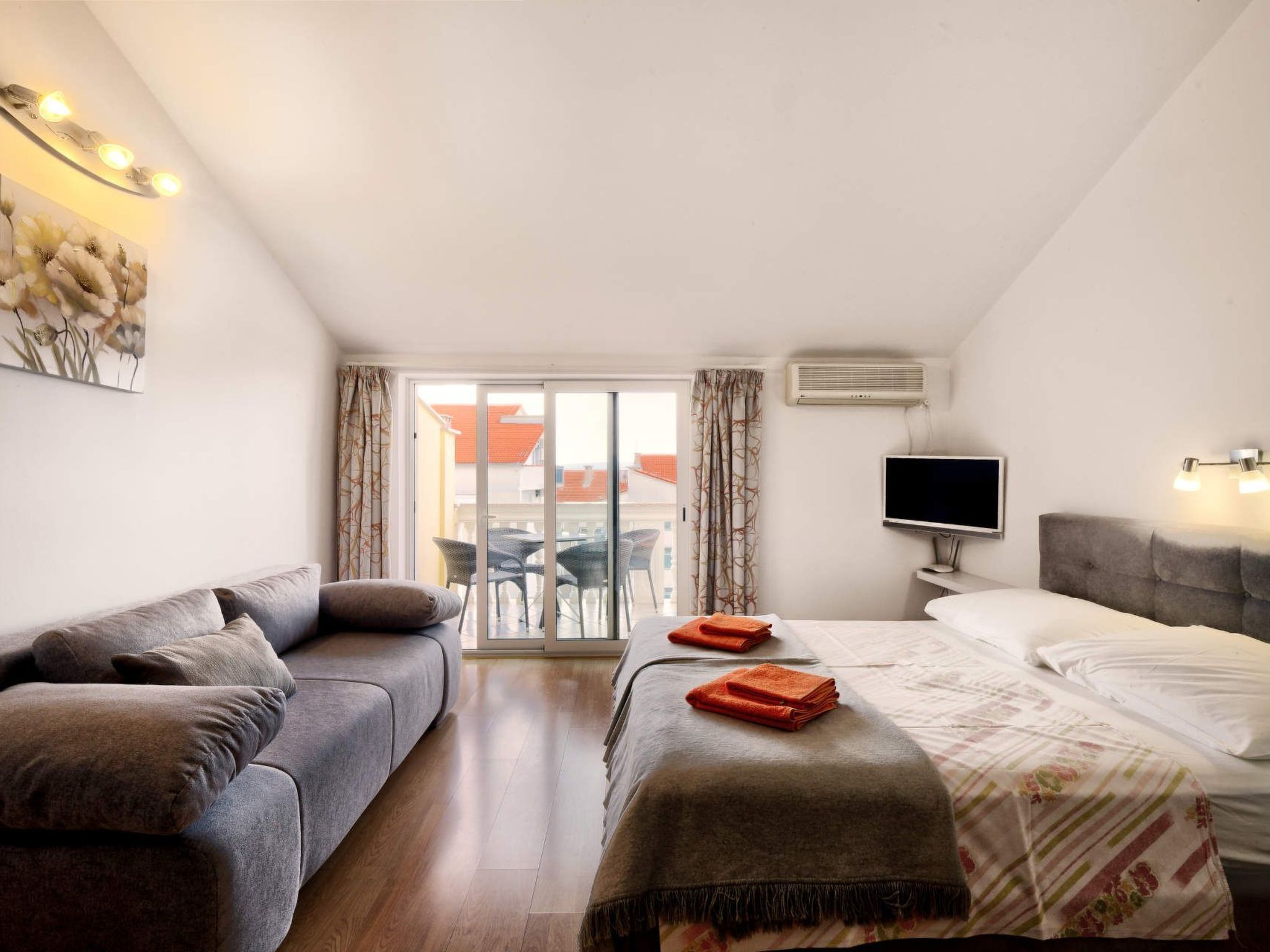 Quarto de hotel com sofá, cama com cobertor, televisão e varanda com cadeiras e mesa.