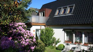 Una casa residencial amb teulada inclinada, un balcó i un jardí ple de plantes florejants.