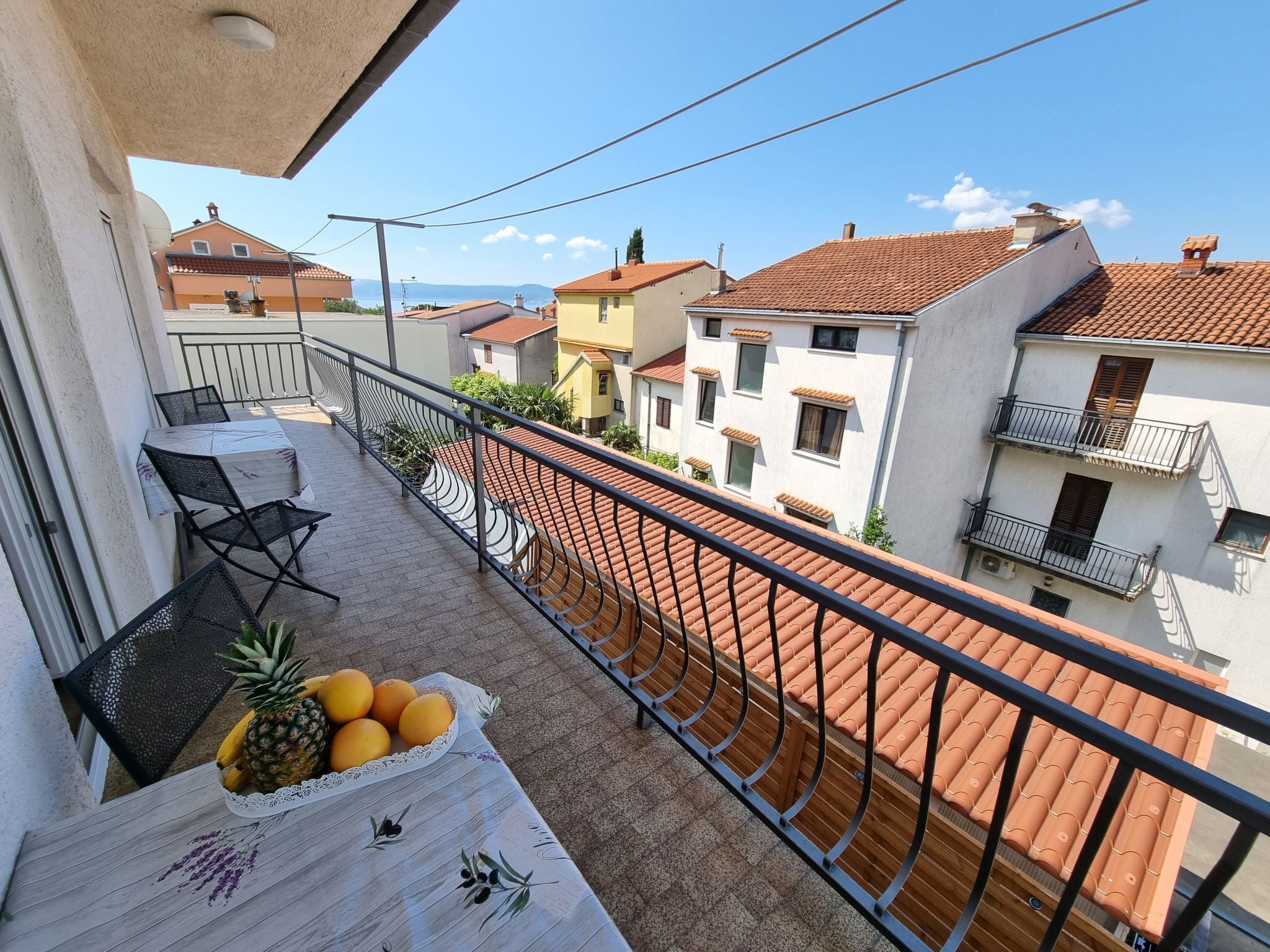 A balcony with a table, chairs, and a fruit bowl containing pineapples and oranges.
