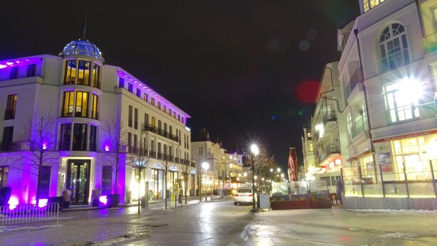 A nighttime street view with illuminated buildings, including a hotel with a dome and a restaurant with a sign. - Domizil für zwei by Interhome (Binz)