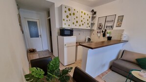 Cocina compacta con microondas, refrigerador y una pequeña isla. Hay un comedor con mesa y sillas, y una sala de estar con sofá y una pequeña mesa redonda.