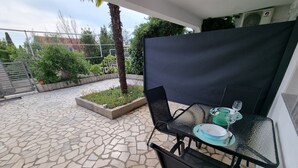 Un patio con mesa y sillas, un pequeño jardín y piso de baldosas de piedra.