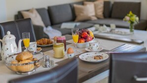 Desayuno preparado para dos personas, con croissants, huevos, fruta y jugo.