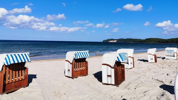 Sillas de playa con toldos a rayas en una playa arenosa con cielo azul despejado y mar tranquilo.