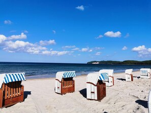Strandstoelen met gestreepte parasols op een zandstrand, met een helderblauwe lucht en een rustige zee.